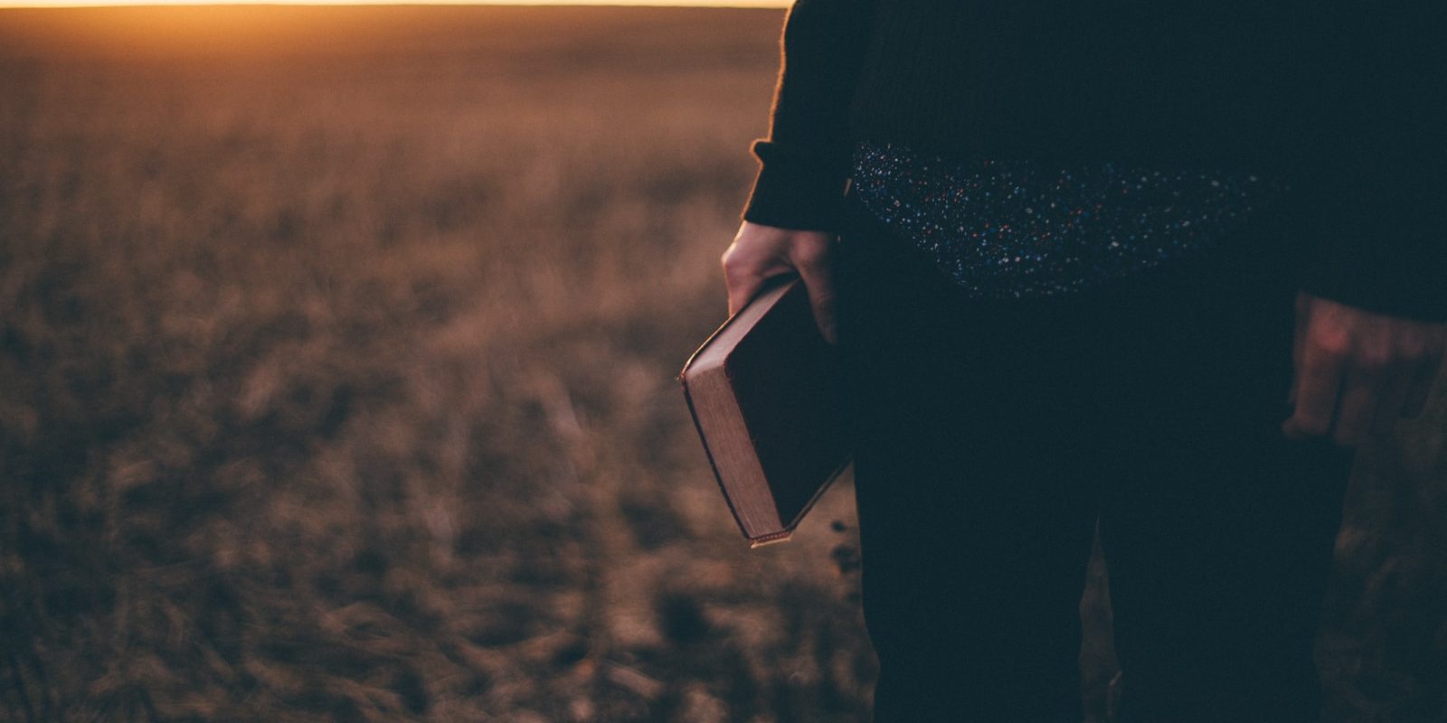 person holding book while standing on field